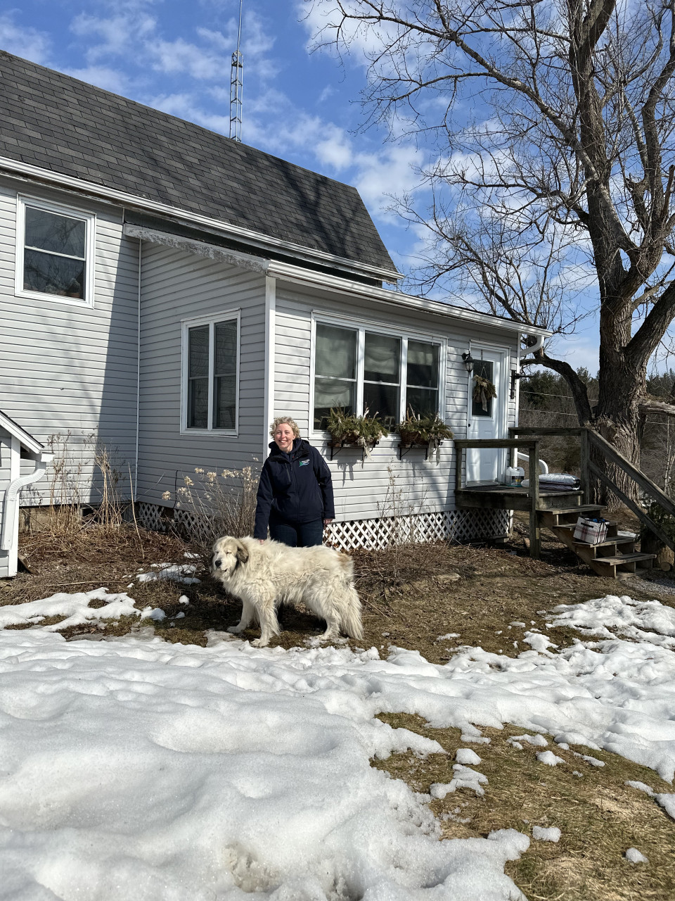 A woman and a large white dog in front of a white farmhouse
