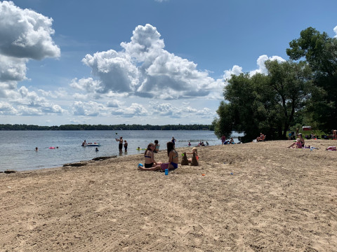 People sit on a sandy beach on a large lake