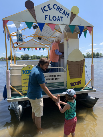 A man and child receive an ice cream cone from a server on a pontoon boat.