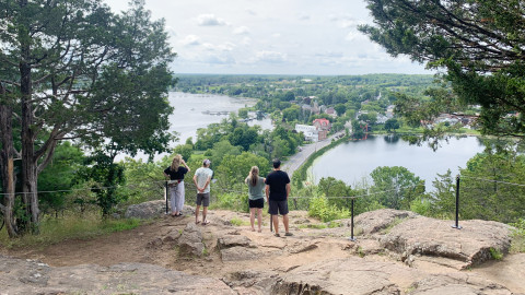 Four people stand on a rocky outcrop overlooking a lake and a town