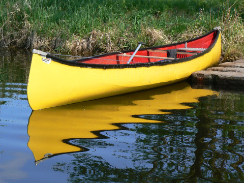 A yellow and red canoe sits in the water tied to a dock