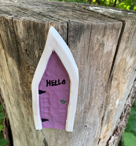 A tiny purple and white door is nailed to a tree stump