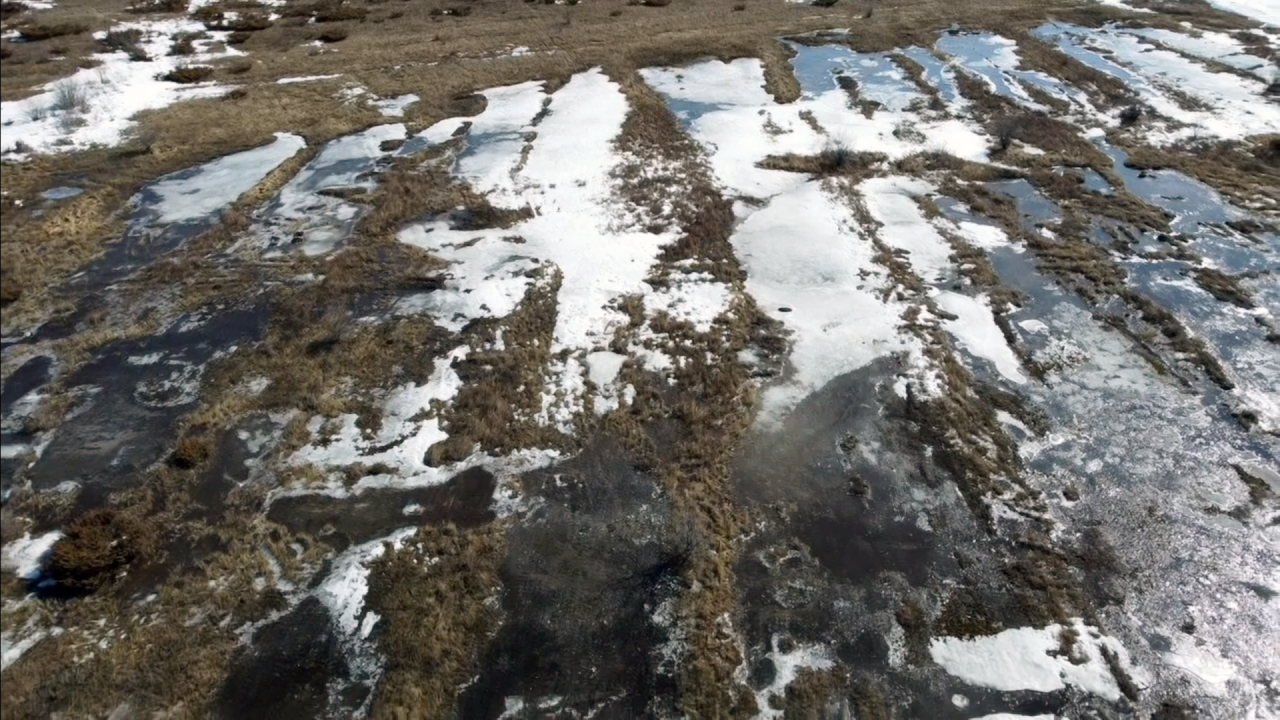 Aerial drone shot of partially snow-covered wetland showing a series of long cracks in the bedrock