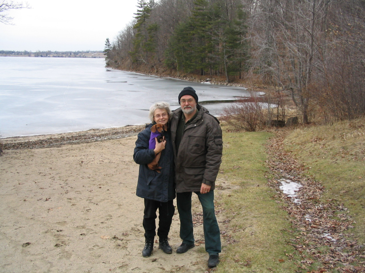 A couple poses for the camera on a beach in front of a frozen lake and shoreline