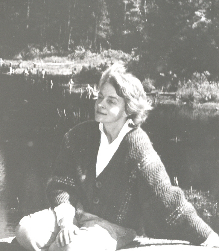 Black and white photo shows young Peri McQuay sitting outside on a rock beside a pond.