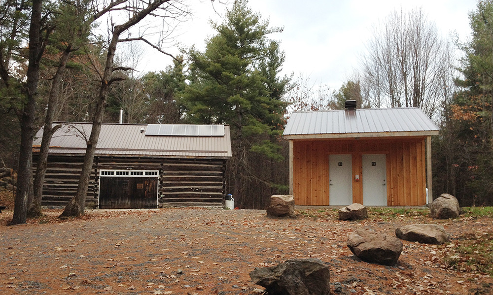 A heritage barn and new outhouse sit in a clearing in the woods